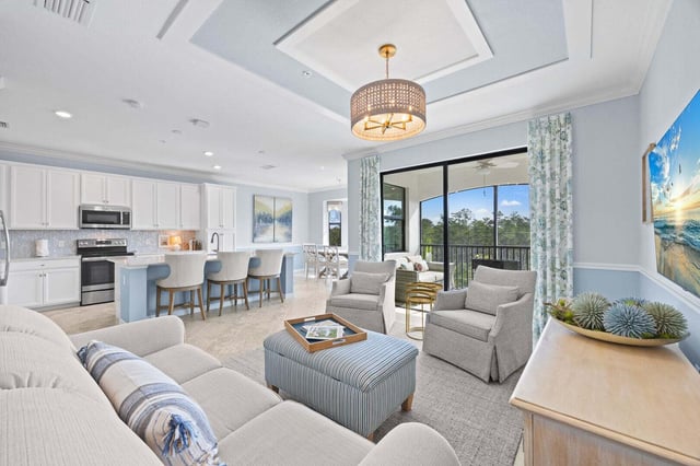 Open-plan condo living room with coastal blue decor, white kitchen island with barstools, and a sunny screened balcony