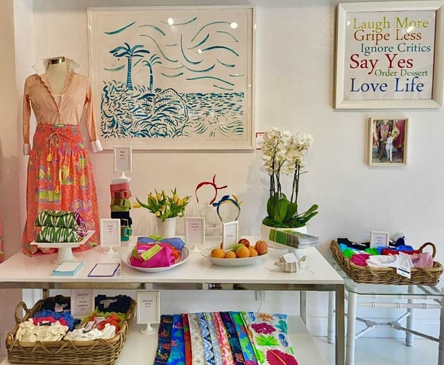 Colorful boutique display at Gretchen Scott with a dressed mannequin, orchids, folded scarves and a Laugh More sign