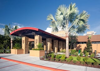 Curved red entry canopy and stone columns at the Seasons 52 restaurant entrance framed by tall palms under blue sky