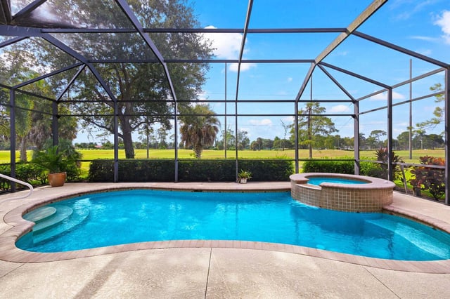 Screened lanai pool and raised spa overlooking a golf course fairway lined with palms under blue sky