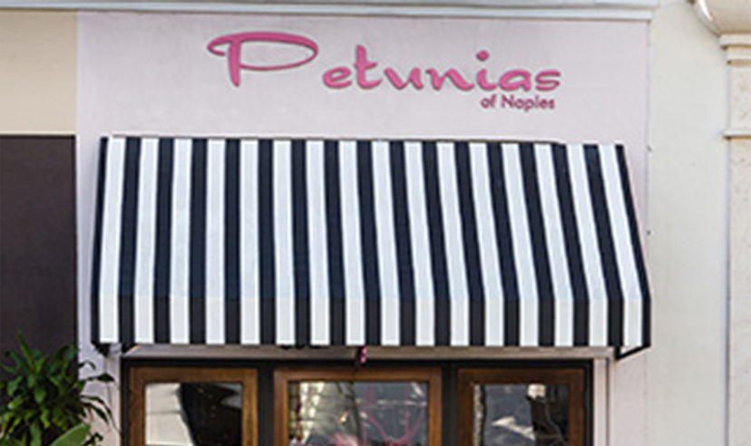Black and white striped awning below the pink Petunias of Naples storefront sign