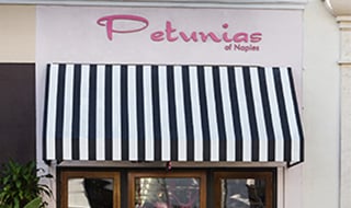 Black and white striped awning below the pink Petunias of Naples storefront sign