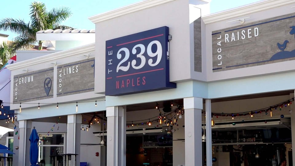 The 239 Naples storefront with navy sign, Local Grown and Local Raised panels, and string lights over the open patio