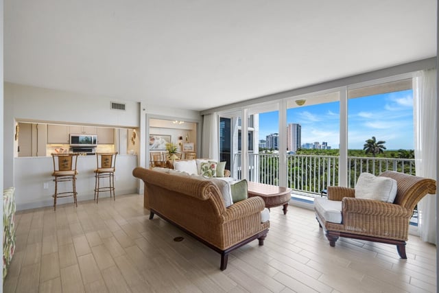 Bright condo living room with wicker sofa and armchairs facing floor-to-ceiling windows overlooking palms and blue sky
