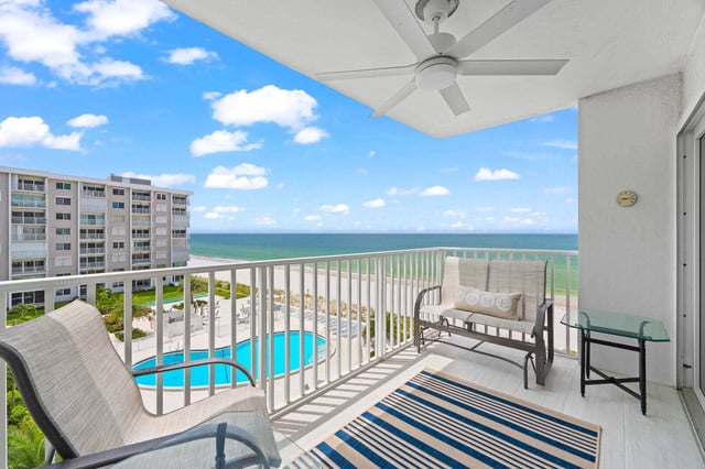 High-rise condo balcony with ceiling fan, striped rug and patio seating overlooking a pool and the Gulf