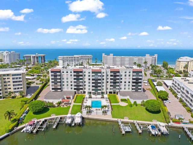 Aerial view of a beachfront condo complex with pool, boat lifts along a canal and the Gulf beyond