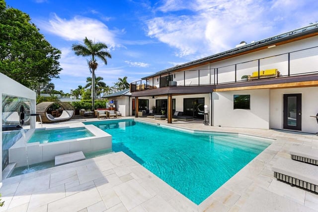 Modern two-story home with turquoise pool, raised spa, water features and palm trees under a blue sky