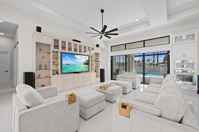 Bright white living room with recliners, built-in media wall and sliding glass doors opening to a screened pool