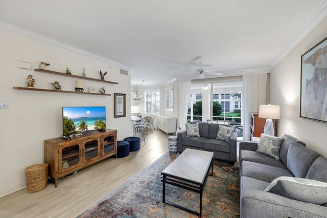 Bright condo living room with gray sofas, wood media console, flat-screen TV and windows overlooking greenery
