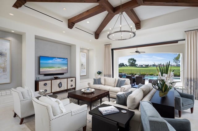 Bright living room with vaulted wood-beam ceiling and iron chandelier opening to a pool and golf course view