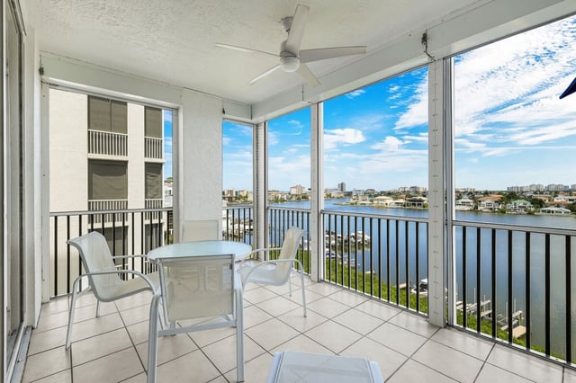 Screened balcony with patio table, chairs and ceiling fan overlooking a wide waterway and waterfront homes