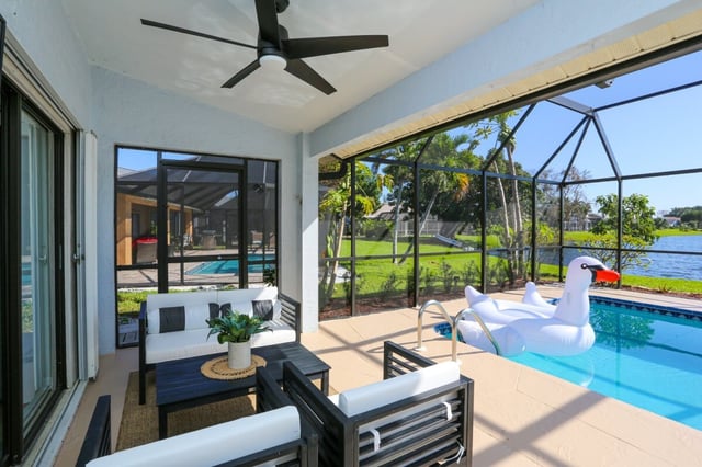 Covered lanai with ceiling fan and patio seating beside a screened pool with a swan float and canal view