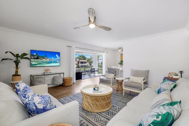 Bright coastal living room with white sofas, tropical print pillows, rattan coffee table and sliding doors to a patio