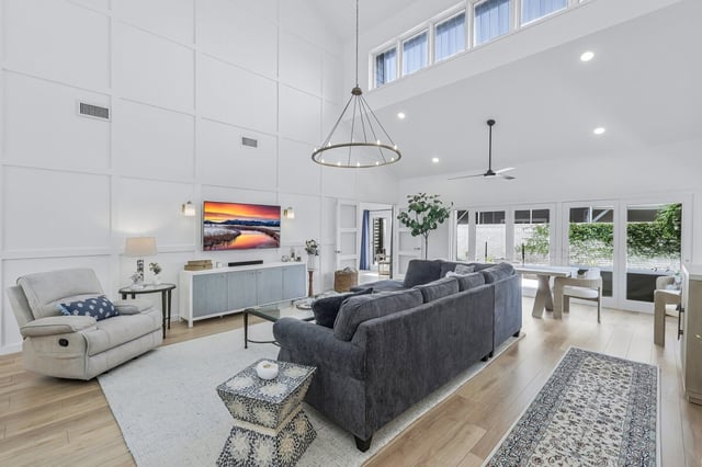 Bright two-story living room with vaulted ceiling, gray sofa, recliner, wall-mounted TV and iron chandelier