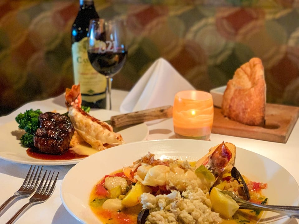 Candlelit table at Bistro 821 set with a seafood stew, filet mignon with lobster tail, bread, and red wine