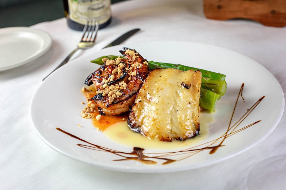 Seared white fish fillet with glazed shrimp, nuts and green beans plated with sauce drizzle at Bistro 821