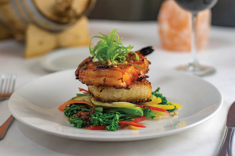 Glazed shrimp over a crisp rice cake with sauteed greens and peppers, plated with red wine at Bistro 821