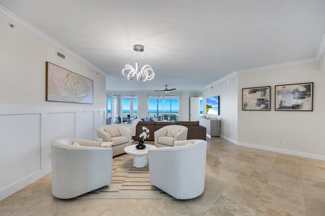 Bright coastal condo living room with cream armchairs, modern chandelier and balcony doors framing a Gulf view