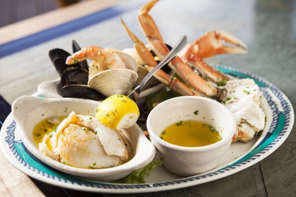 Seafood platter with crab claws, mussels, clams, shrimp, white fish and drawn butter on a blue-rimmed plate
