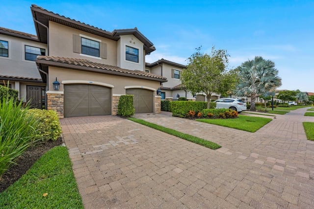Mediterranean-style townhomes with tile roofs, attached garages and brick paver driveways in a landscaped community