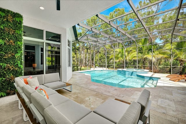 Screened lanai with a pool, spa and travertine deck beside a white sectional sofa and living green wall