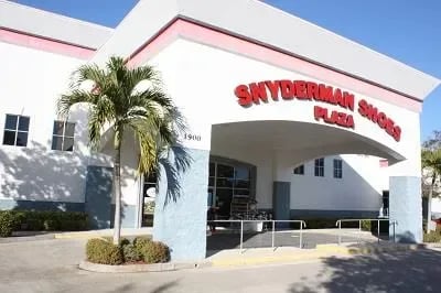 Exterior of Snyderman Shoes Plaza with pink and white stucco, red lettering, and palm trees out front