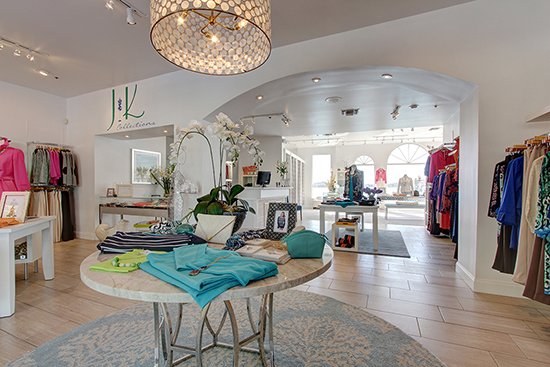 Bright boutique interior at J&K Collections with folded turquoise clothing on a round table, orchids and racks of apparel