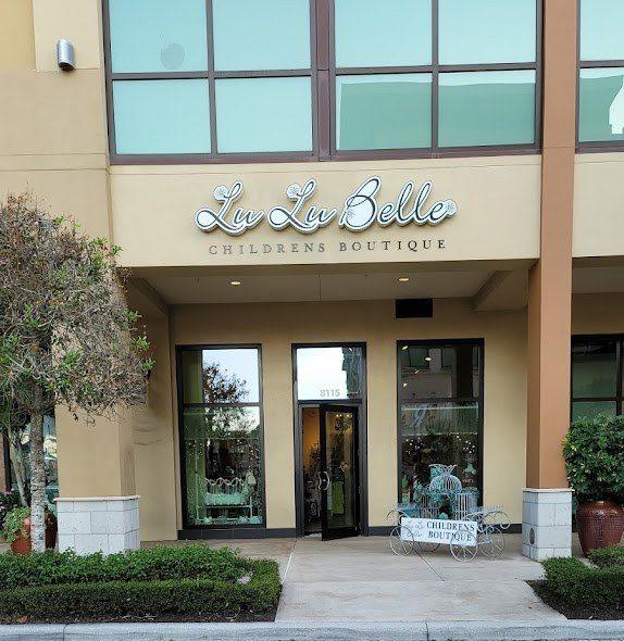 Storefront of Lu Lu Belle Childrens Boutique with script signage, glass display windows and a white carriage cart out front