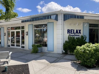 White Tommy Bahama storefront with blue striped awnings, shutters and RELAX lettering under a bright blue sky