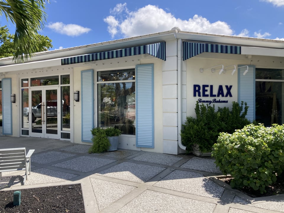 White Tommy Bahama storefront with blue striped awnings, shutters and RELAX lettering under a bright blue sky