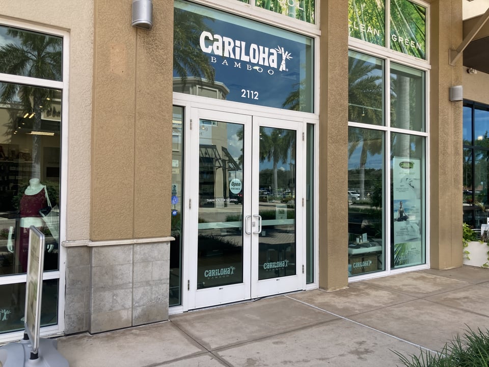 Glass storefront entrance of Cariloha Bamboo at suite 2112, with palm trees reflected in the windows