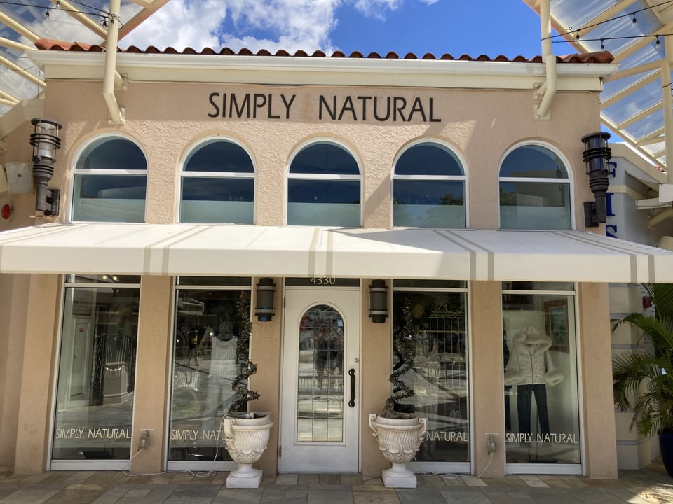 Storefront of Simply Natural with arched windows, white awnings and urn planters flanking the entrance