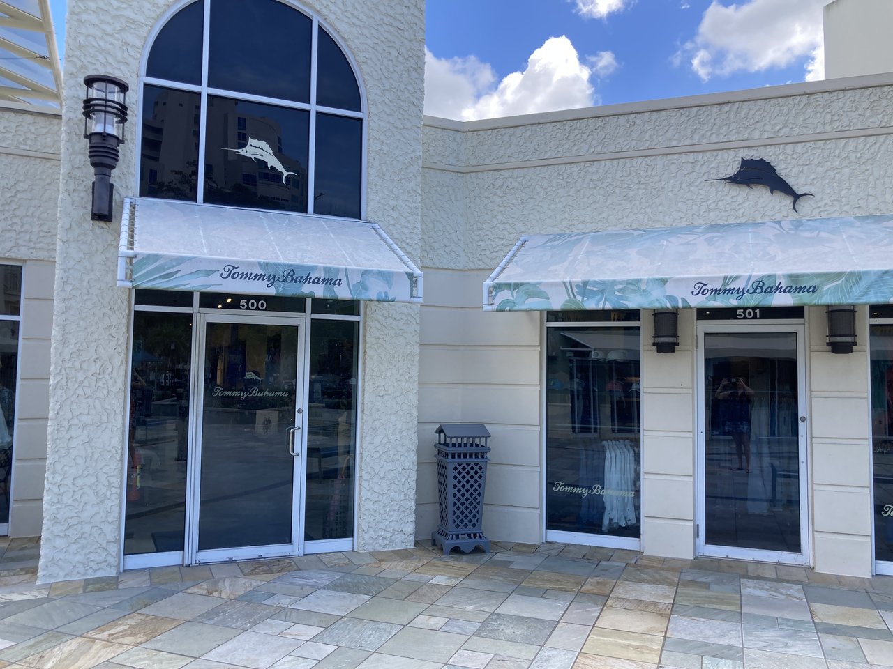 Tommy Bahama storefront with palm-print awnings and marlin logos along a tiled walkway at the Village Shops