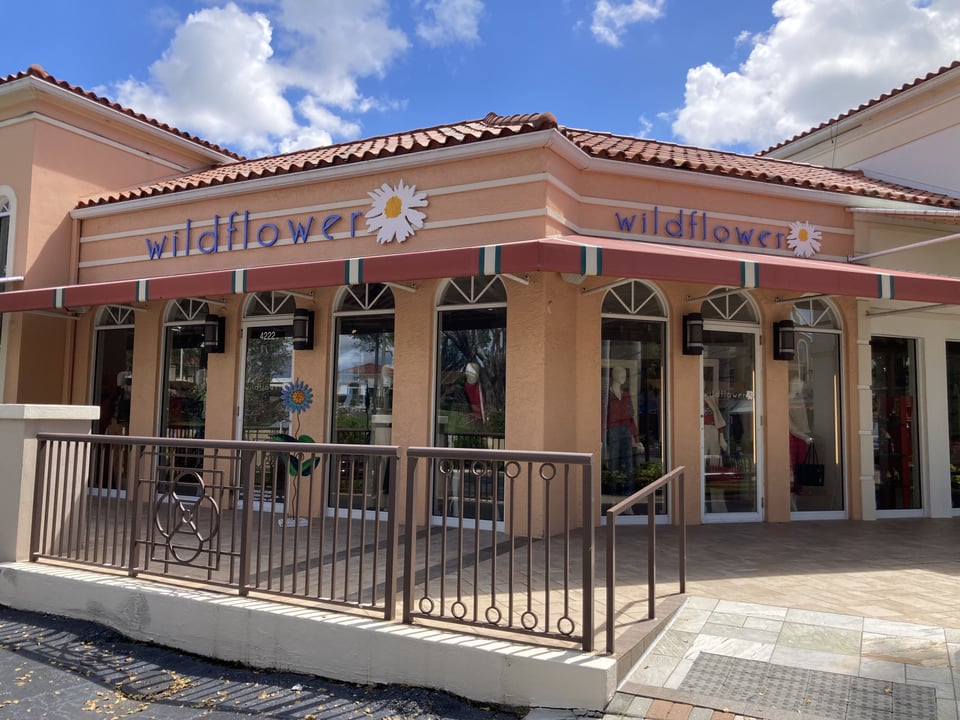 Exterior of Wildflower boutique with peach stucco walls, daisy signage and window displays under a blue sky