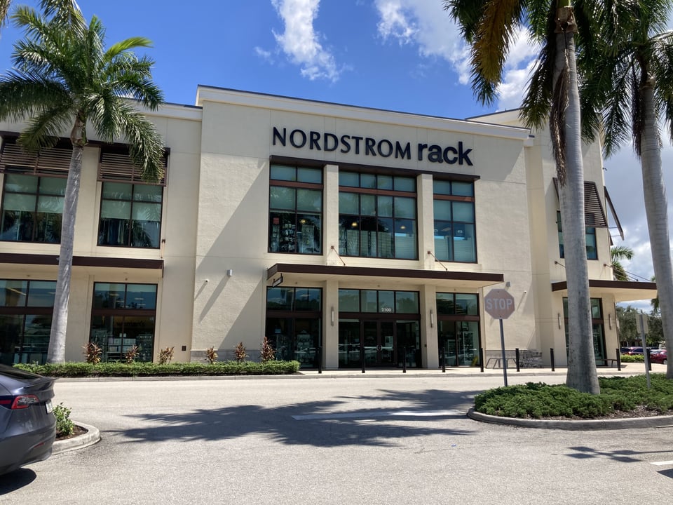 Nordstrom Rack storefront with tall glass windows framed by palm trees under a bright blue sky