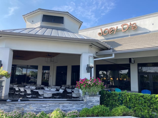 Exterior of Joey D's Italian Restaurant with covered patio seating, pink flowers and blue sky
Sorry, something went wrong