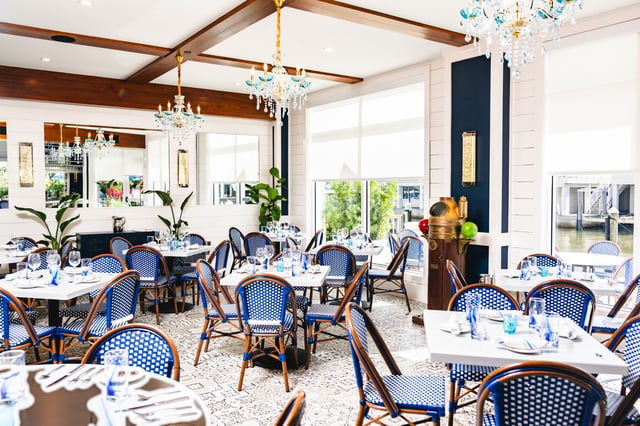 Bright dining room at The Syren Oyster & Cocktail Bar with blue bistro chairs, wood beams and glass chandeliers