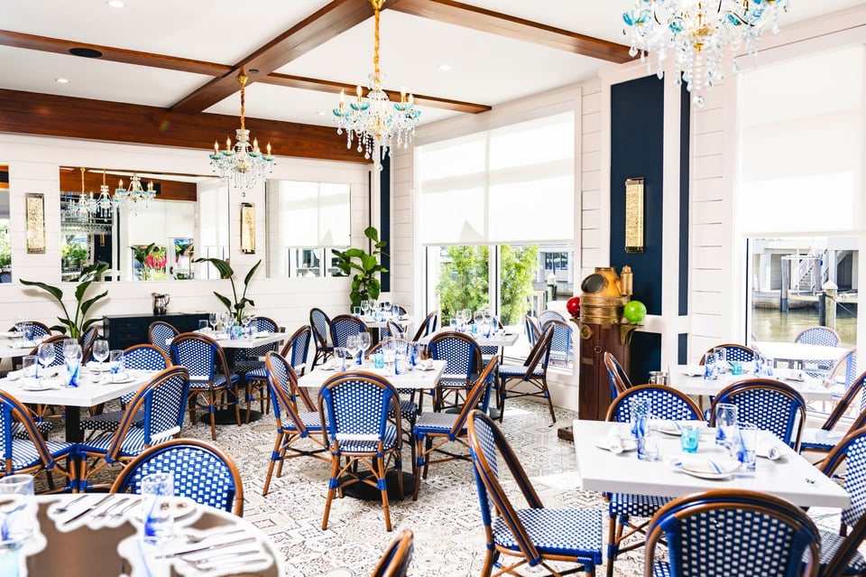 Bright dining room at The Syren Oyster & Cocktail Bar with blue bistro chairs, wood beams and glass chandeliers