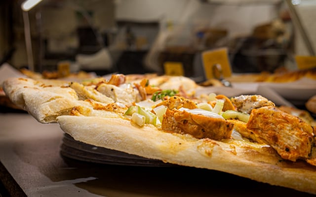 Thick-crusted pizza topped with grilled chicken, celery and ranch drizzle on a pan at a pizzeria counter