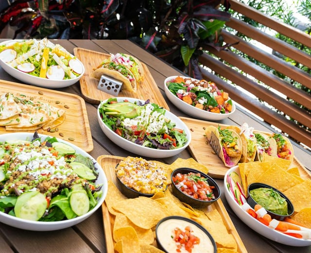 Overhead view of tacos, salads, quesadilla, chips and dips arranged on wooden trays on a patio table