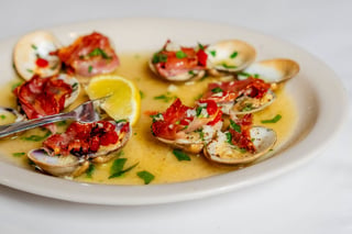 Plate of steamed clams in lemon garlic butter broth topped with crispy prosciutto, parsley and diced red pepper