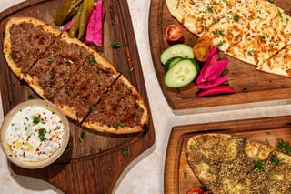 Overhead view of lamb flatbread, cheese flatbread and za'atar manakish on wooden boards with pickles and yogurt dip