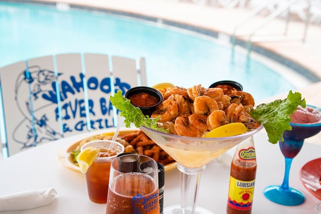 Peel-and-eat shrimp in a giant martini glass beside drinks, with a Wahoo's branded chair and pool behind