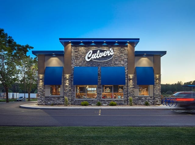 Culver's stone-fronted restaurant with blue awnings and lit windows at dusk