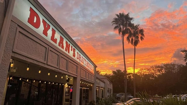 Dylan's Drafthouse storefront with string lights under a vivid orange sunset sky and tall palm trees