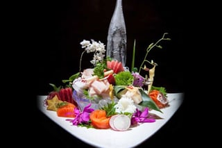 Elaborate sashimi platter with salmon, tuna and white fish, orchids and an ice sculpture bottle on black