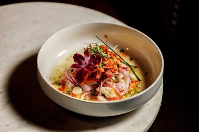 Colorful ceviche topped with orchid petals and crispy carrot in a white bowl on marble