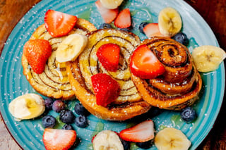 Cinnamon swirl pastries topped with strawberries, banana and blueberries on a turquoise plate