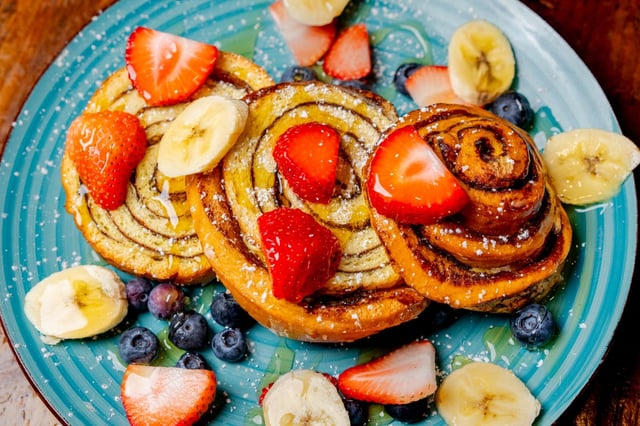 Cinnamon swirl pastries topped with strawberries, banana and blueberries on a turquoise plate