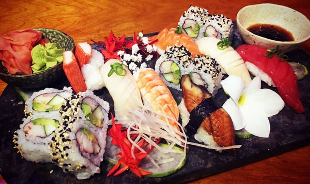 Assorted sushi platter of rolls and nigiri on a dark slate with ginger, wasabi and flowers